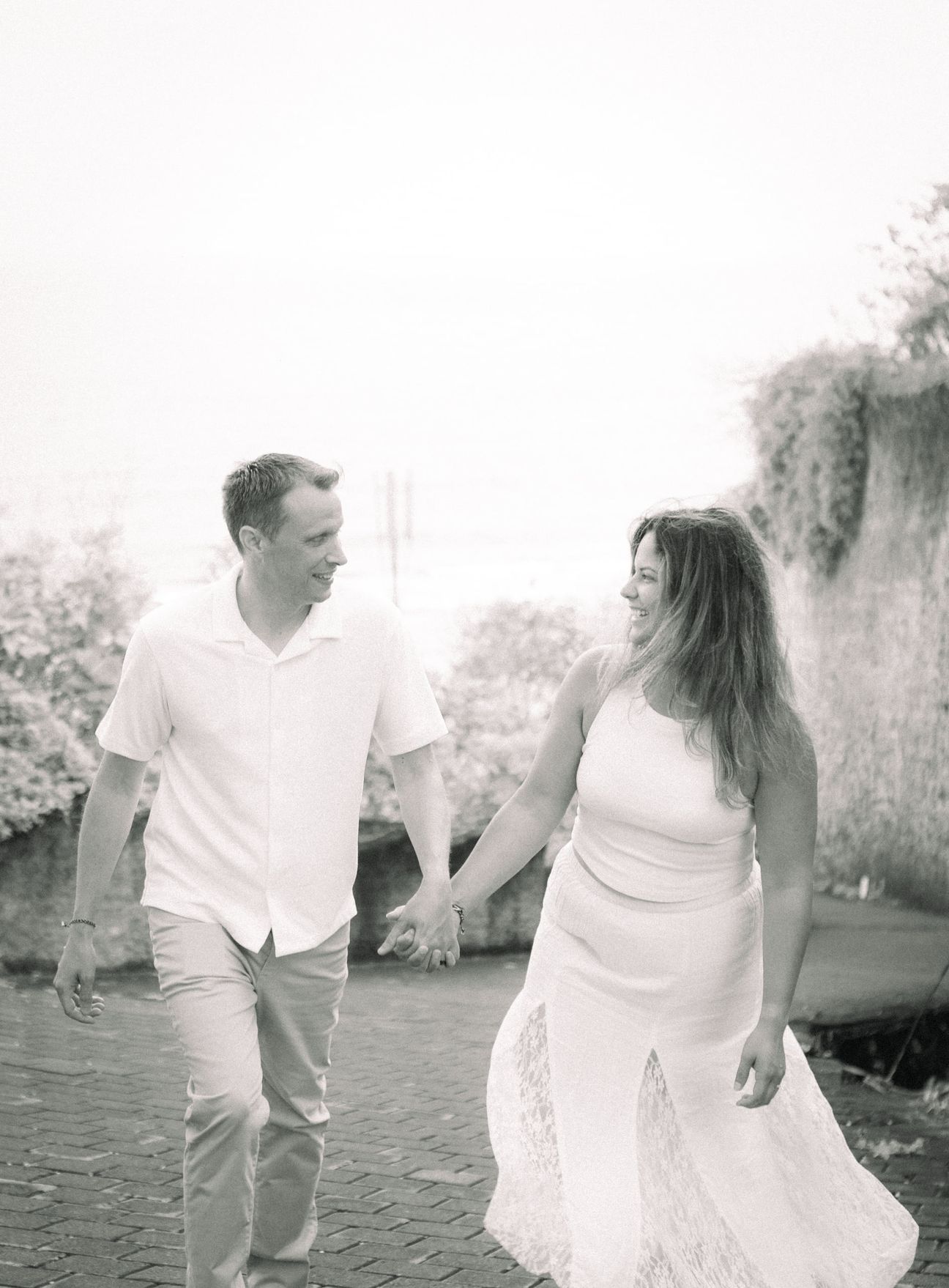 An expectant couple walk hand in hand in soft daylight
