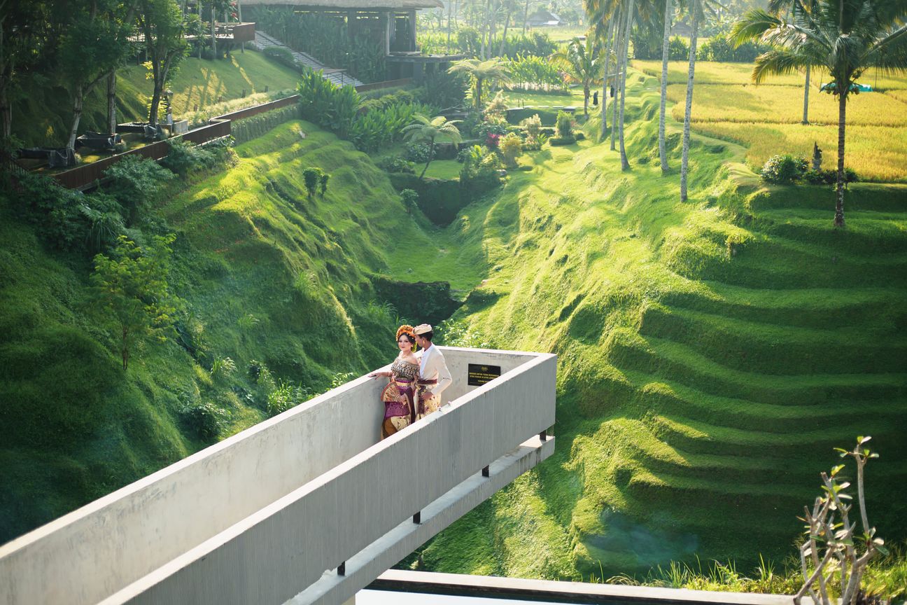 A couple stand together on a modern walkway overlooking green rice terraces