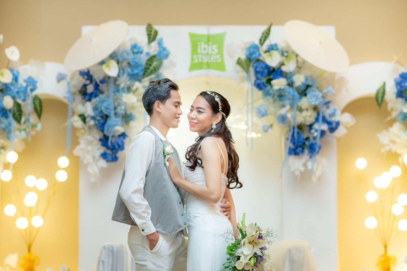 A bride and groom smile together before a floral wedding backdrop