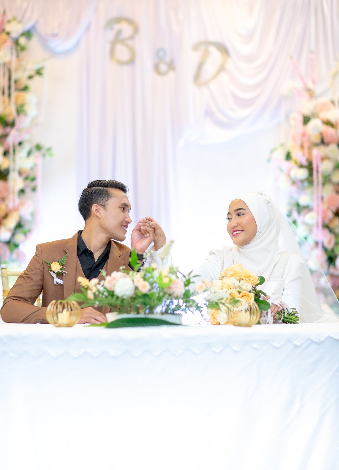 A bride and groom smile together before a floral wedding backdrop