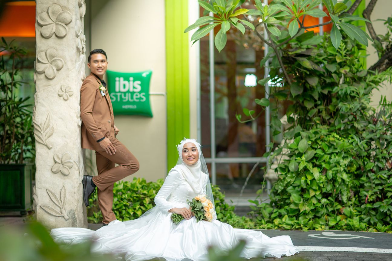 A bride and groom smile together before a floral wedding backdrop