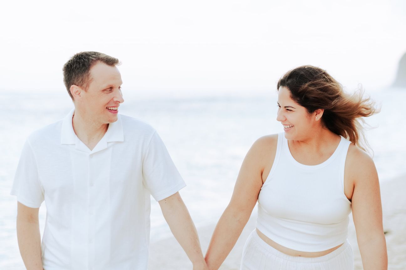 A couple embrace and walk together on a beach near sunset