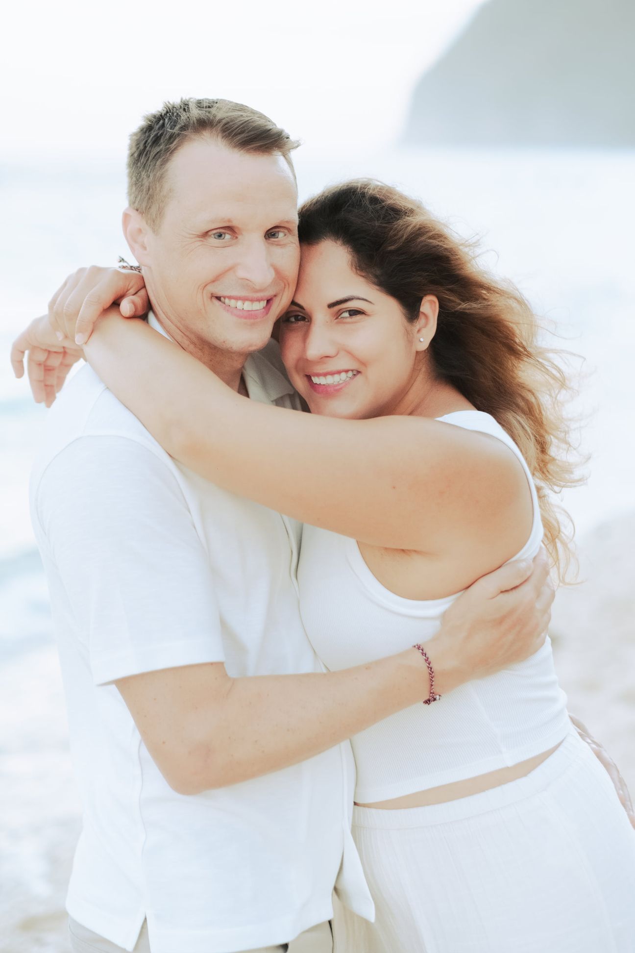 A couple embrace and walk together on a beach near sunset