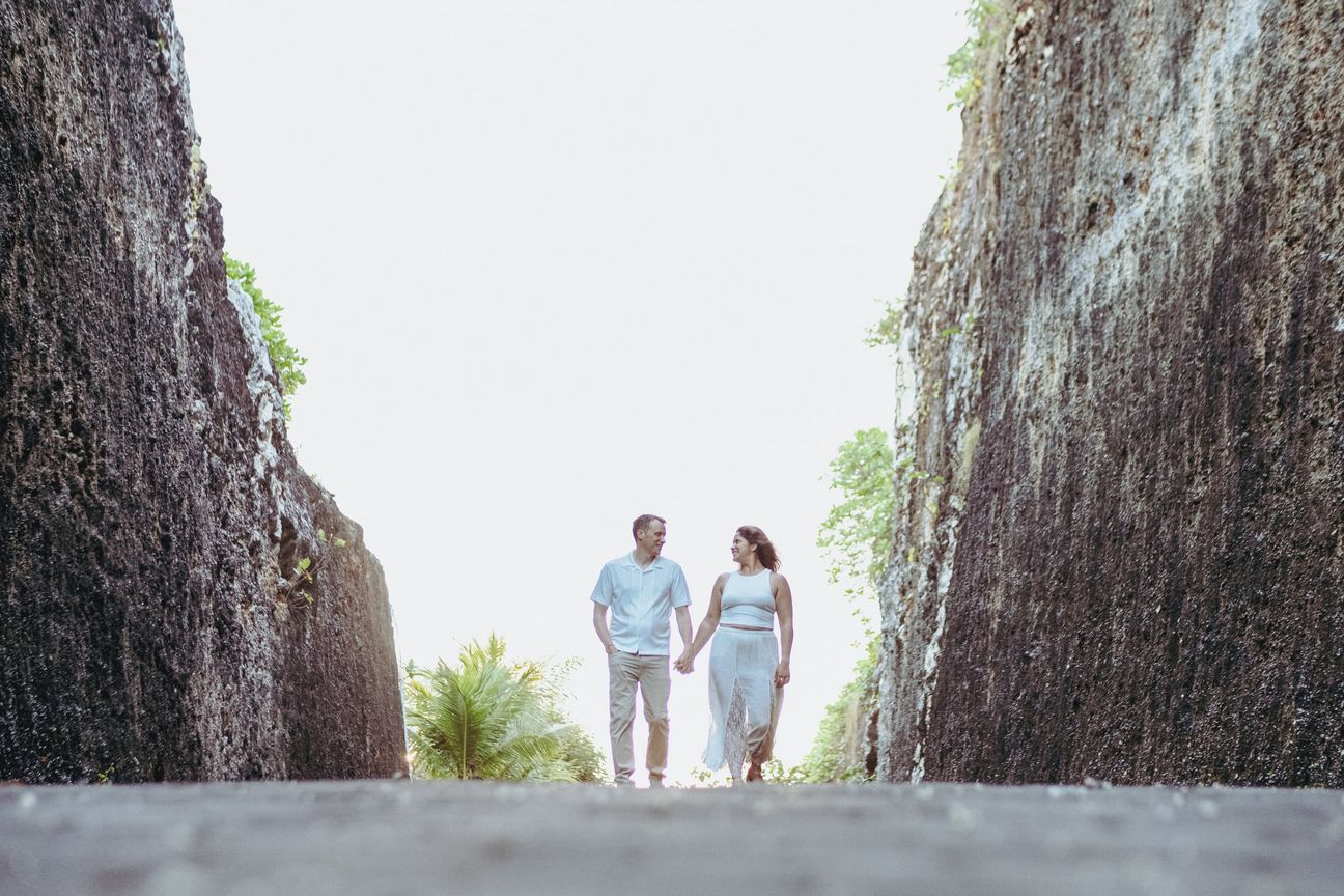A couple walk hand in hand through a narrow stone passage