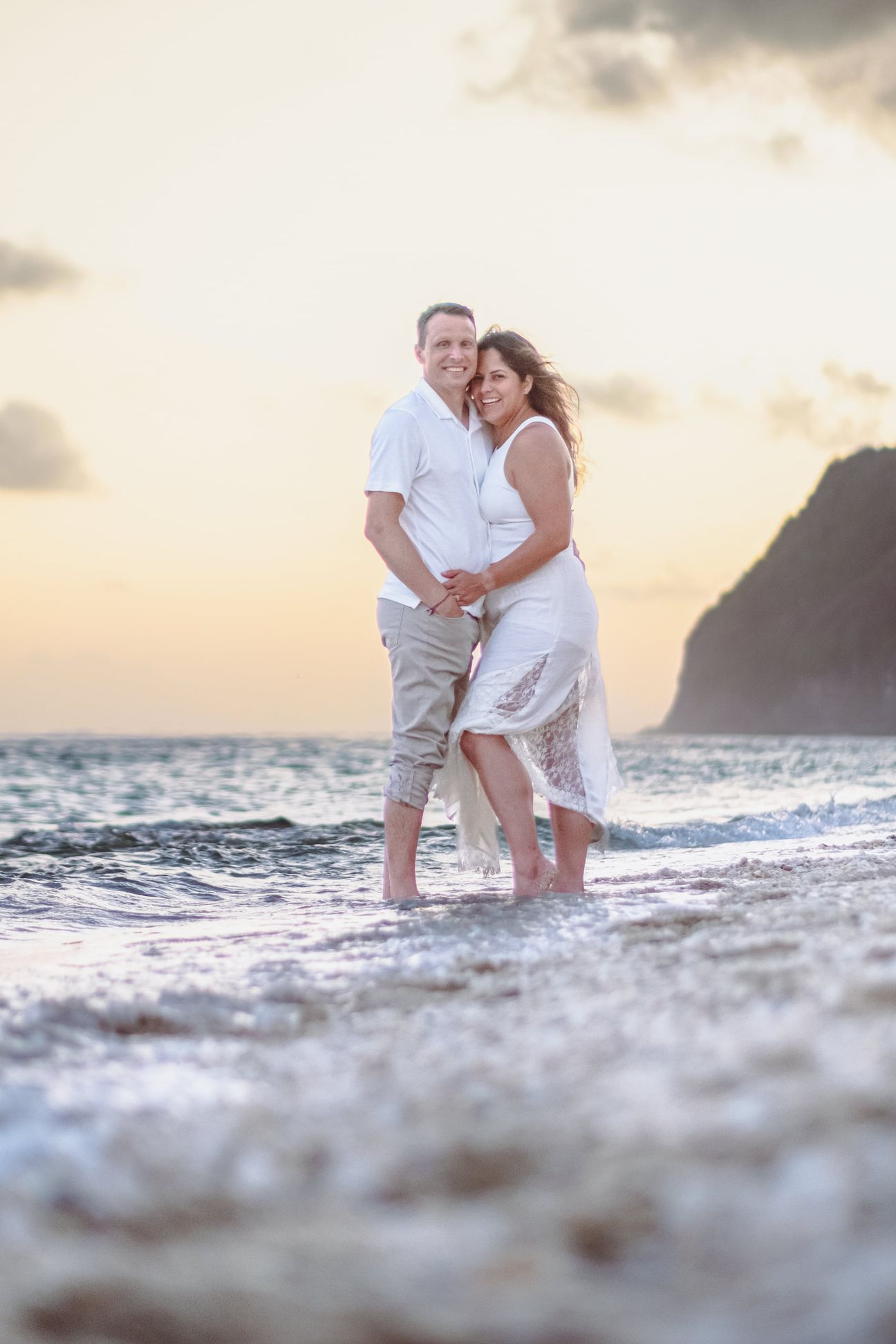 A couple embrace on wet sand with the sea behind them