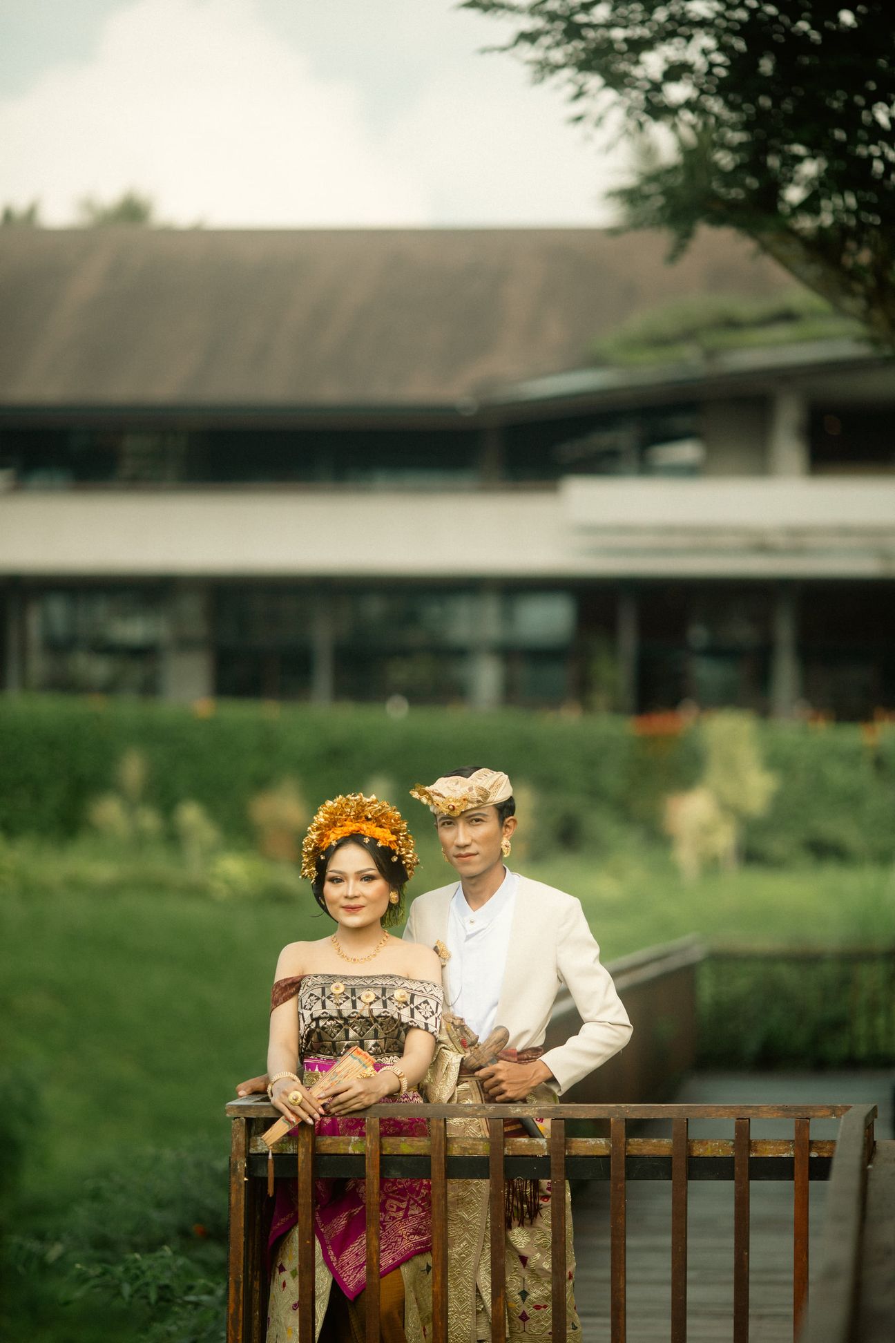 A couple in Balinese attire pause together beside a peaceful garden pavilion