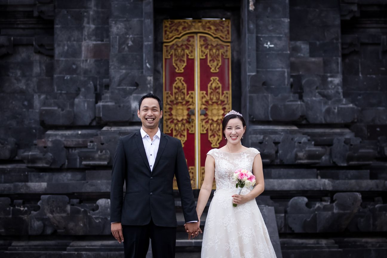 A bride and groom embrace along a wooden boardwalk through leafy mangroves