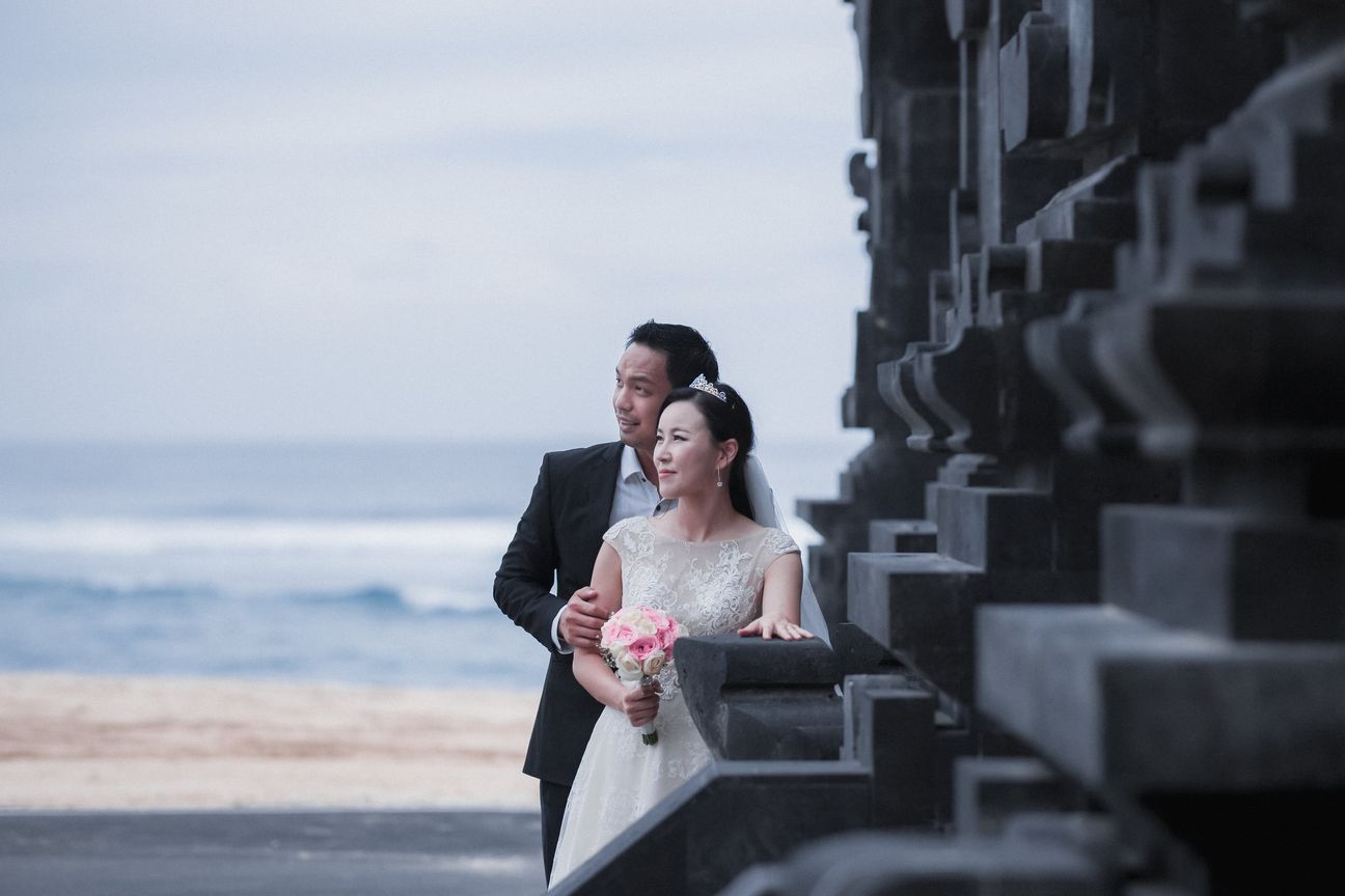 A bride and groom embrace along a wooden boardwalk through leafy mangroves