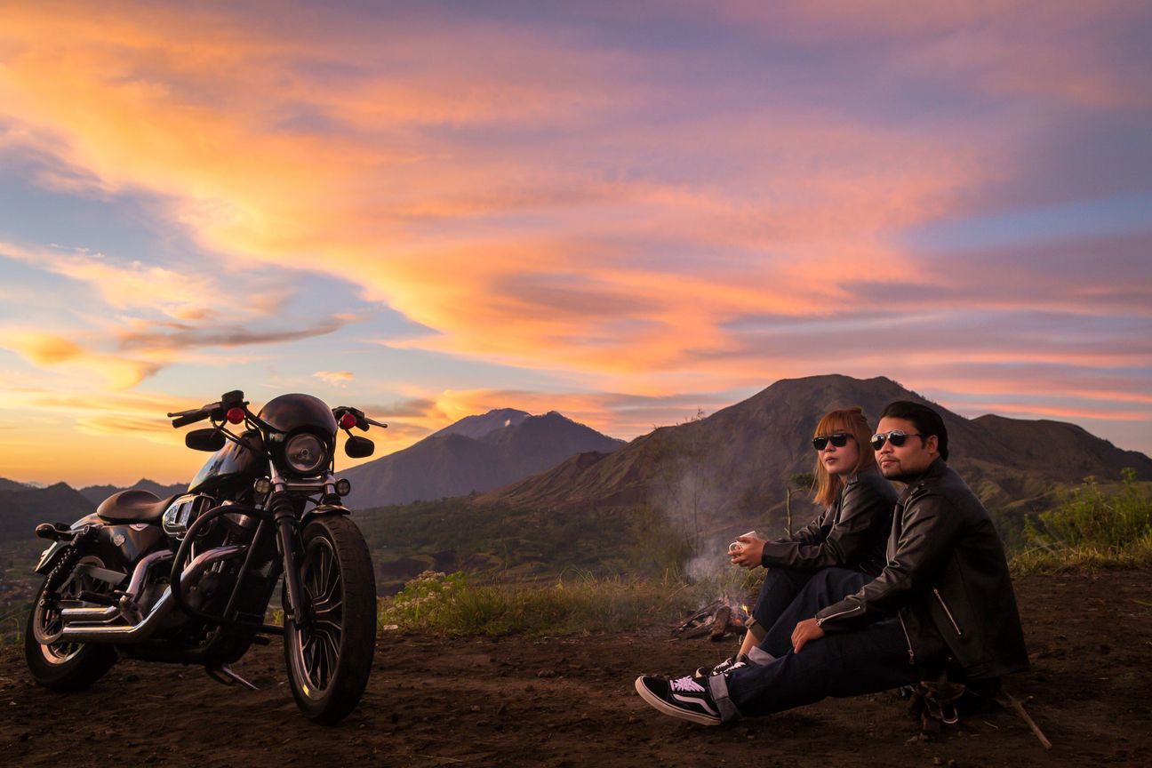 A couple pause with a motorcycle against a mountain landscape