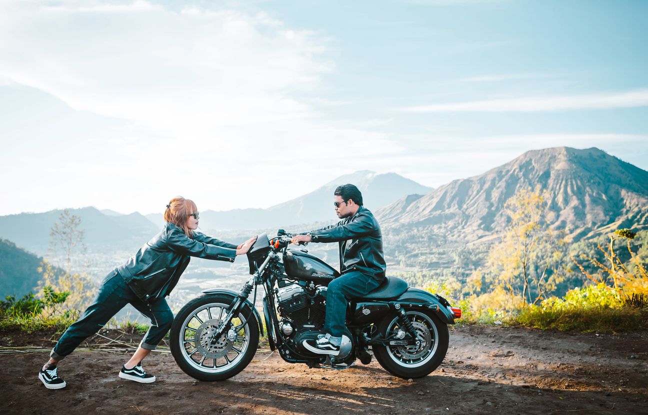 A couple pause with a motorcycle against a mountain landscape