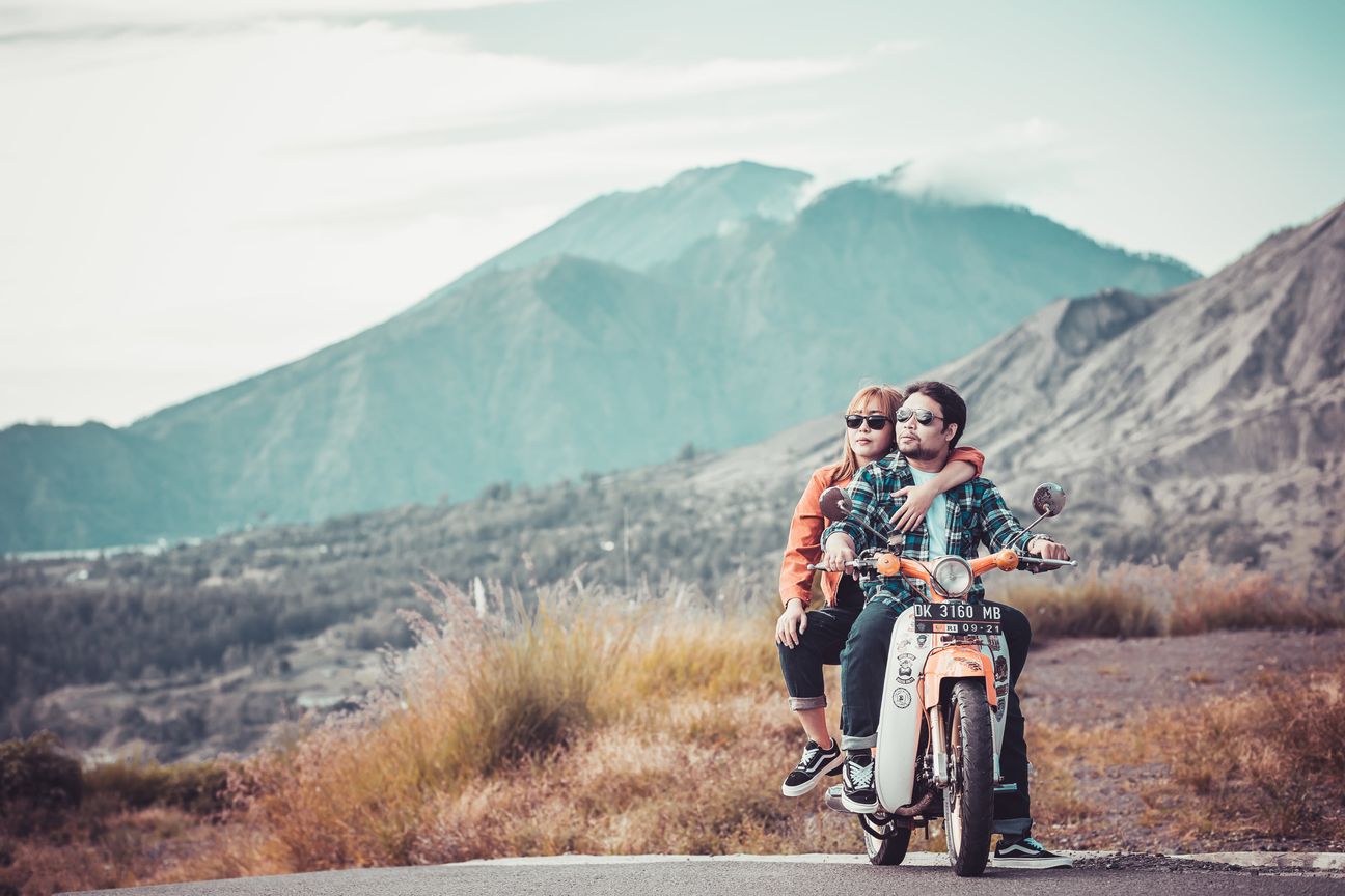 A couple pause with a motorcycle against a mountain landscape