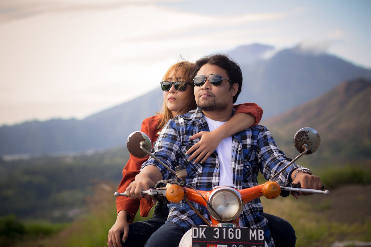 A couple pause with a motorcycle against a mountain landscape