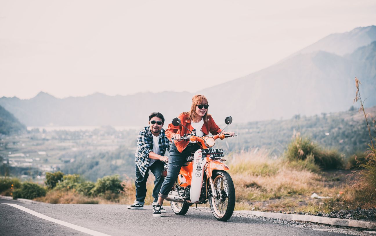 A couple pause with a motorcycle against a mountain landscape