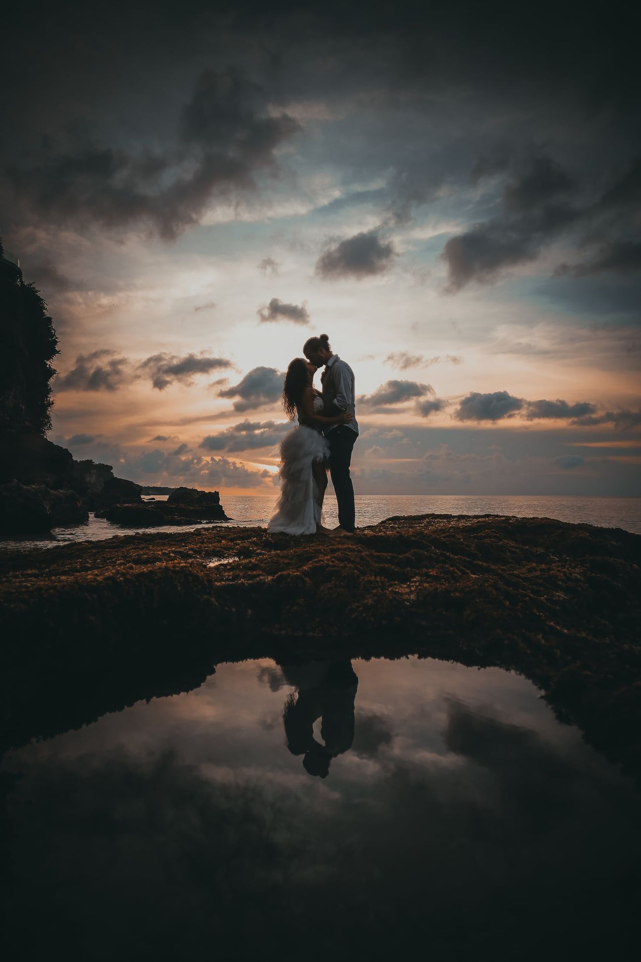 A couple stand in silhouette beneath a dramatic evening sky