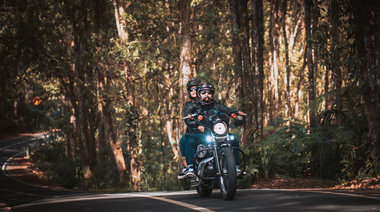 A couple ride a motorcycle together along a forest road