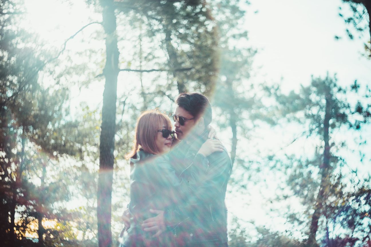 A couple face one another beneath sunlit trees