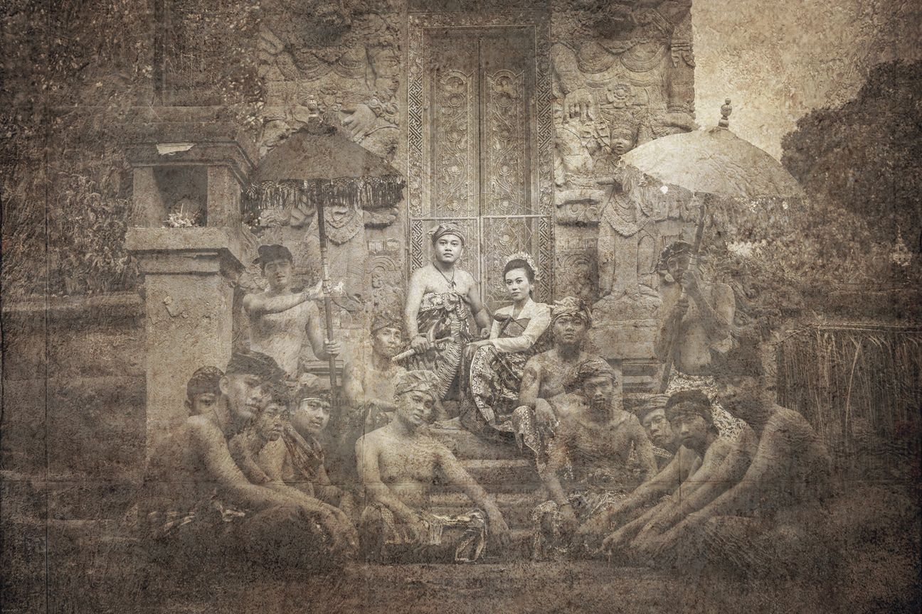 A royal Balinese wedding couple seated with their ceremonial entourage in vintage sepia tones
