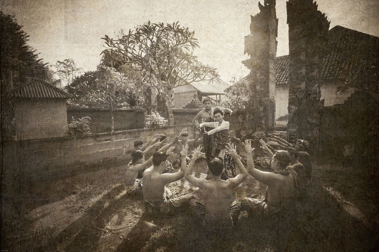 A royal Balinese wedding couple seated with their ceremonial entourage in vintage sepia tones
