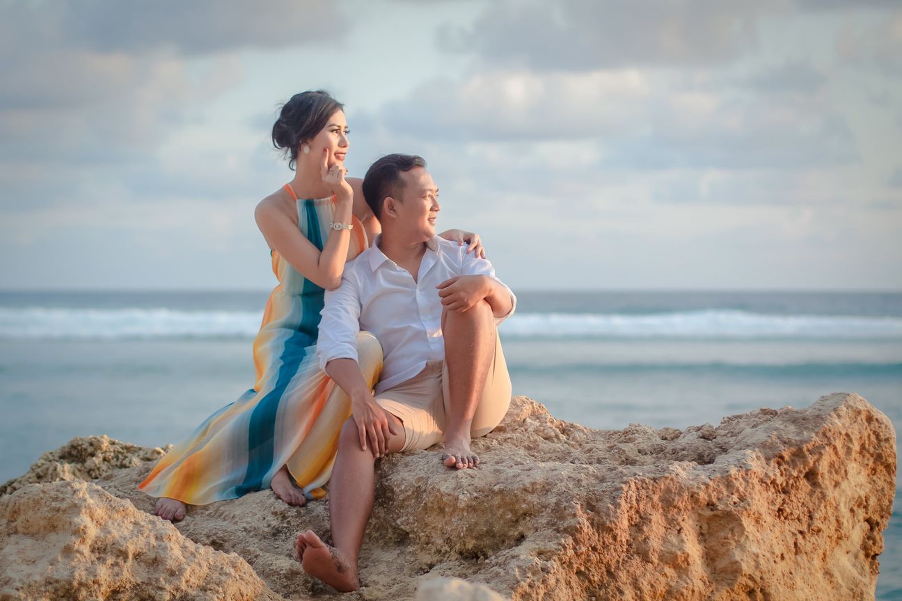 A couple sit together on coastal rocks in warm evening light