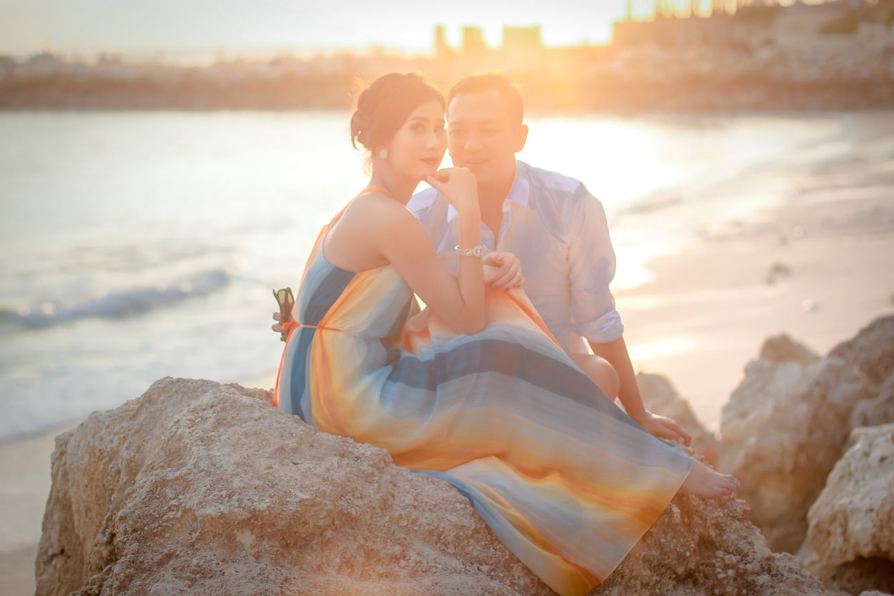 A couple sit together on coastal rocks in warm evening light
