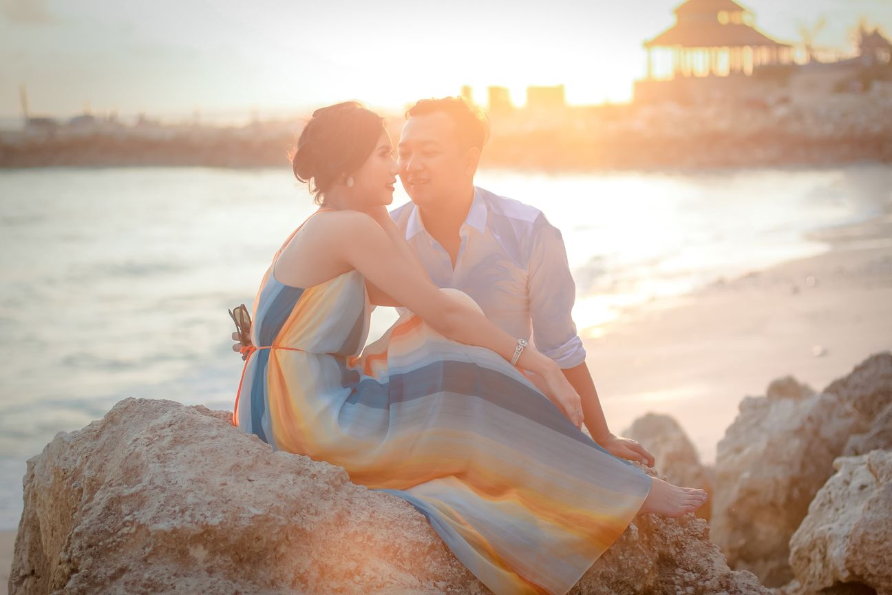 A couple sit together on coastal rocks in warm evening light