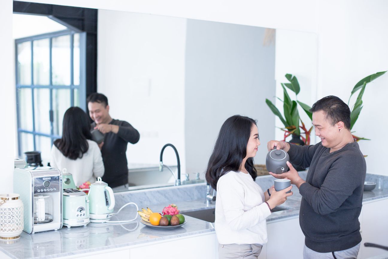 A couple laugh together while preparing food in a bright kitchen