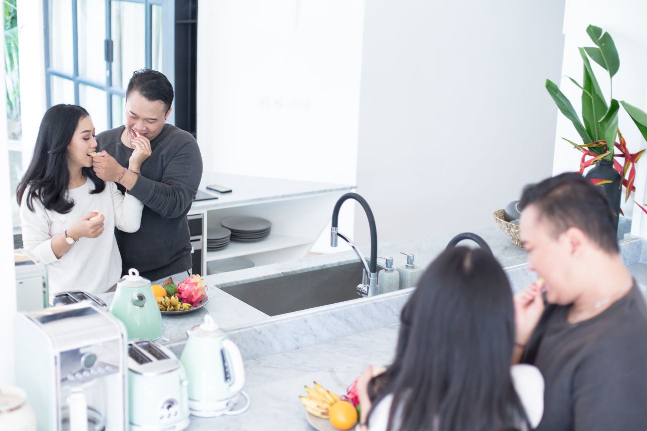 A couple laugh together while preparing food in a bright kitchen
