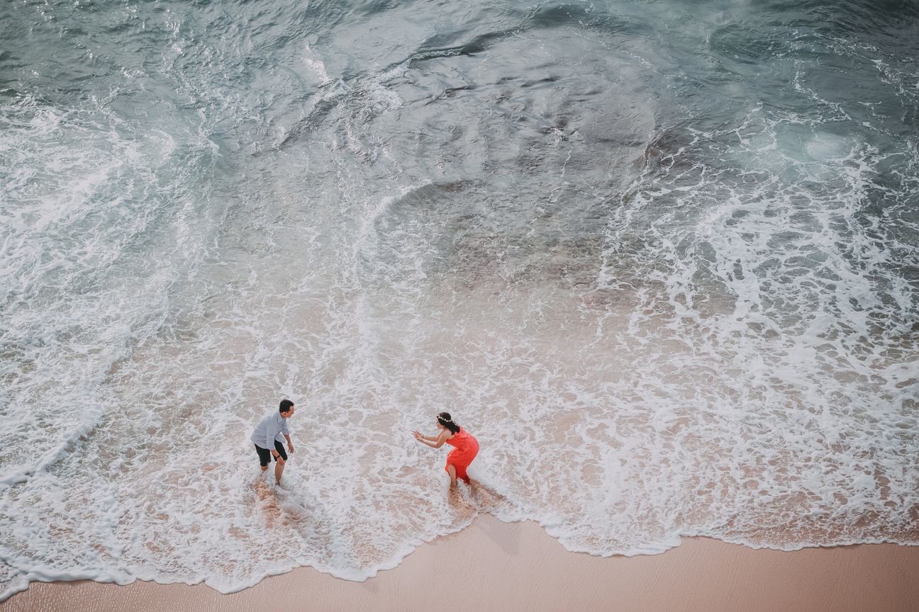 An aerial view shows two people walking beside a breaking wave