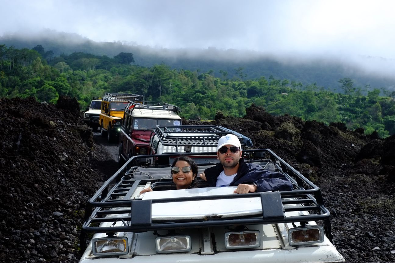 Two guests lean out of an open-topped jeep, the rest of the convoy climbing the lava field behind them