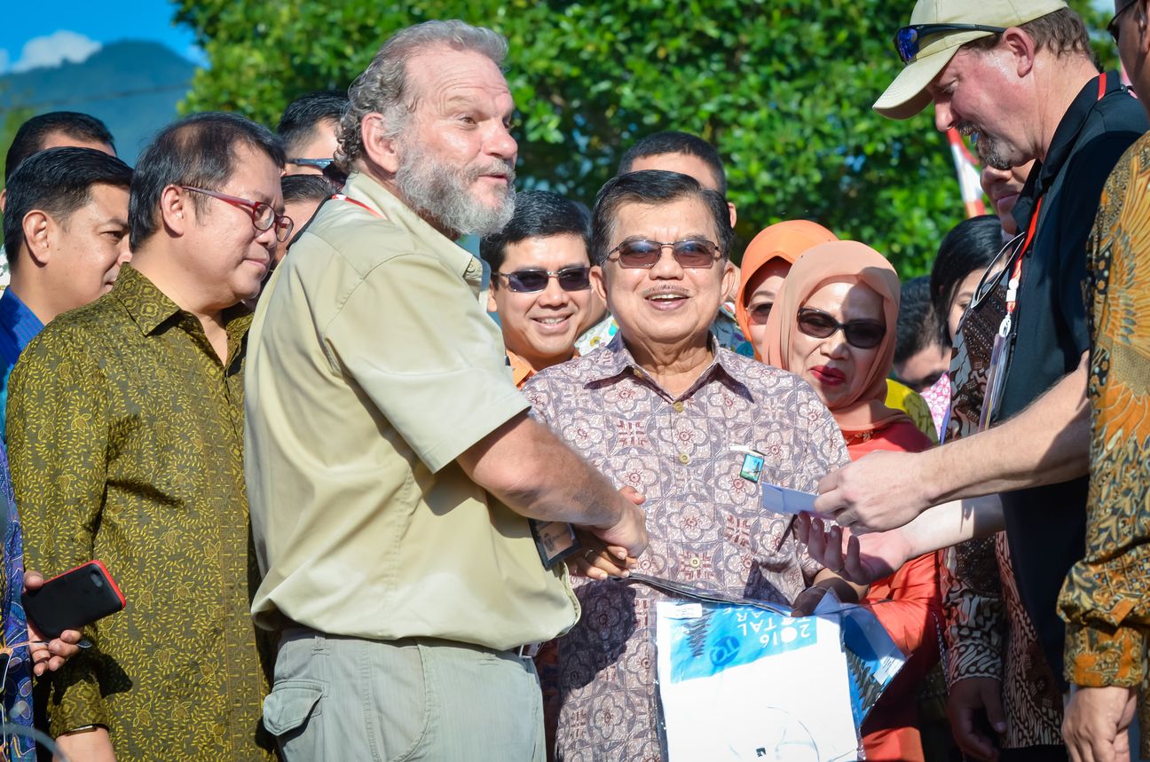 Two men shake hands in the middle of a crowd, both of them laughing