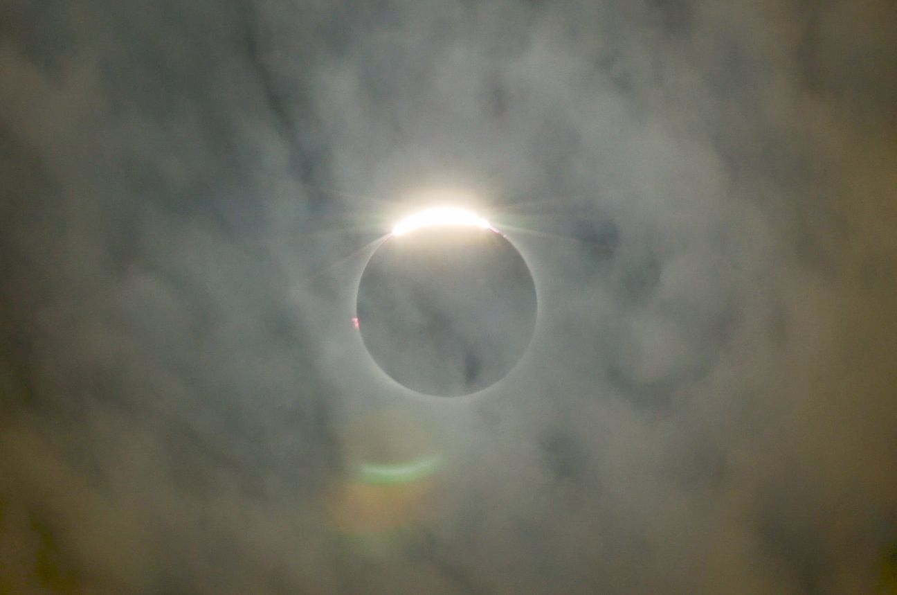 The last bead of sunlight flaring at the moon’s edge through thin cloud