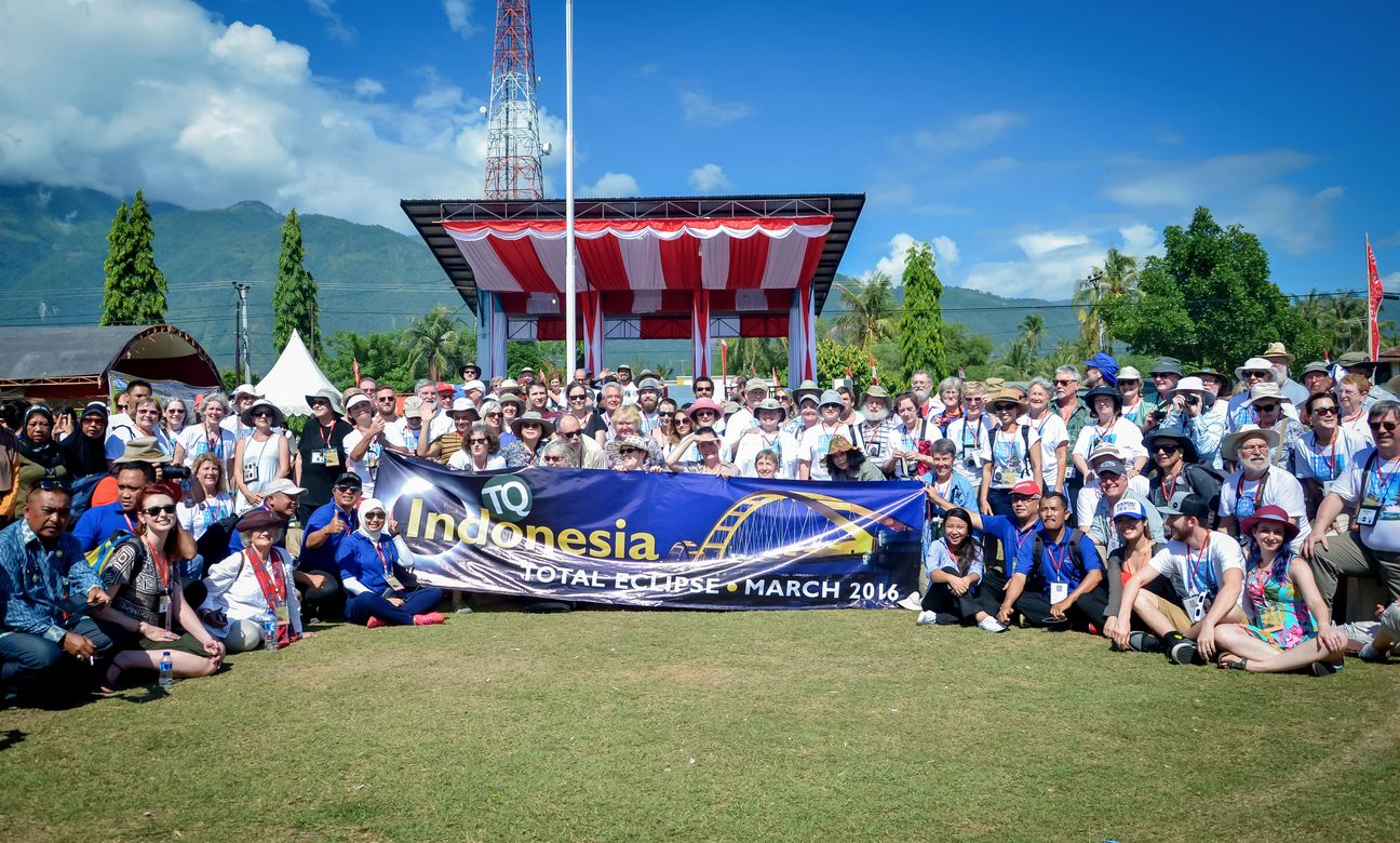 A tour group of about a hundred sits and stands behind a banner reading Indonesia Total Eclipse March 2016