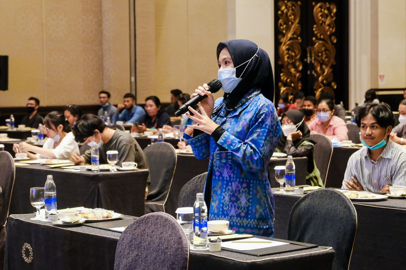 A delegate in blue ikat stands among the tables to ask a question into the microphone