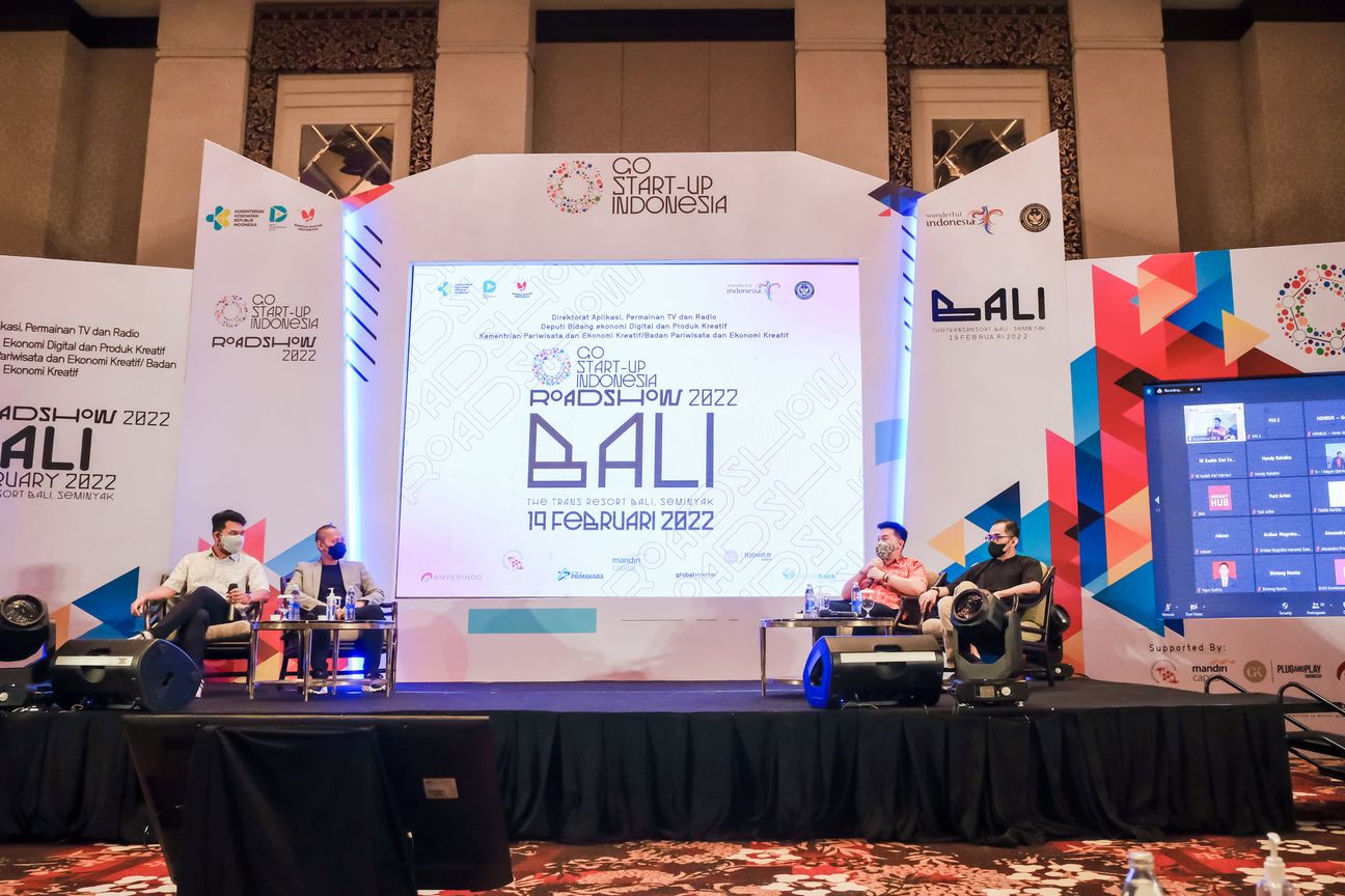 Four panellists seated across a wide stage under the roadshow backdrop