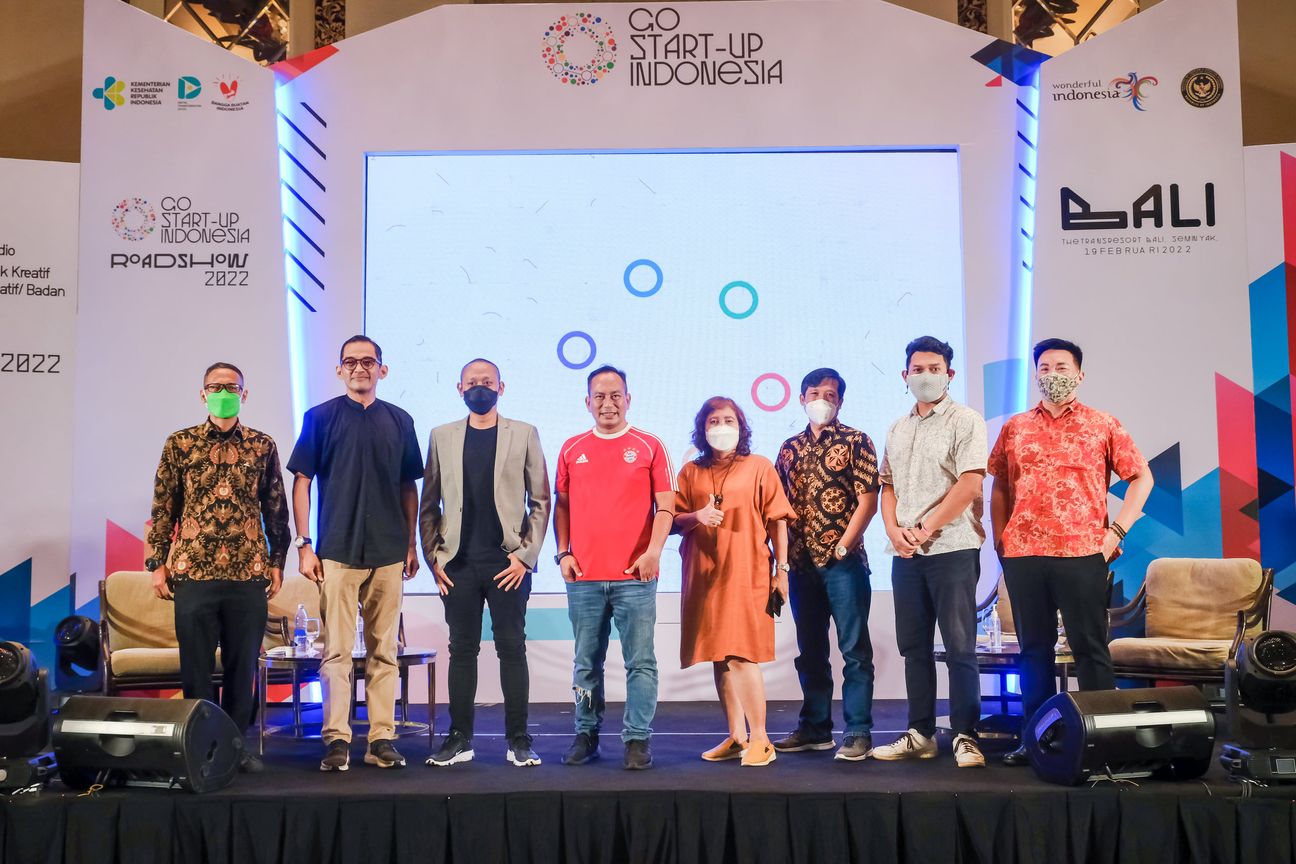 Eight speakers line up across the stage in front of the roadshow screen
