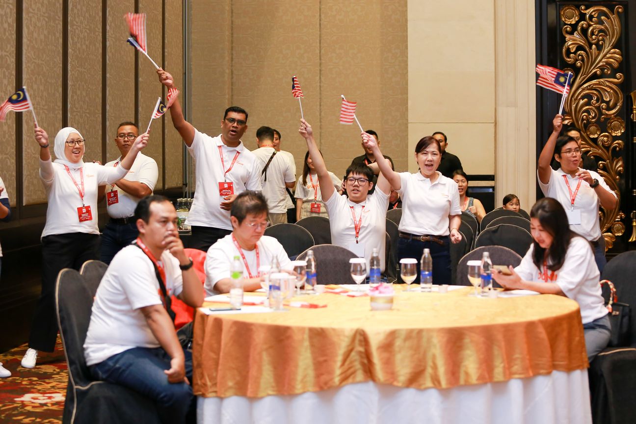 A table of guests in white shirts stand and wave small flags