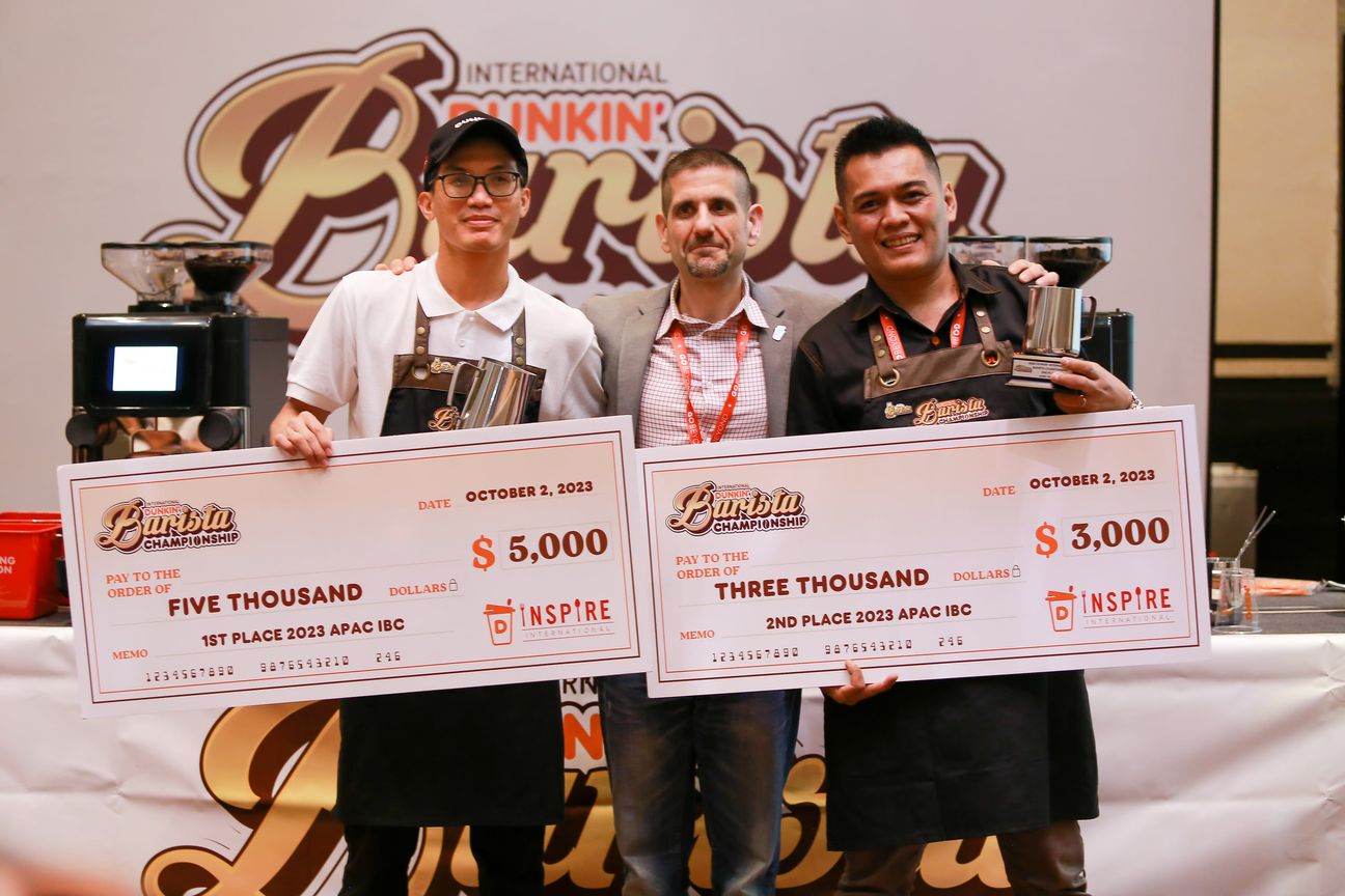 Two baristas hold their cheques and trophies either side of an organiser