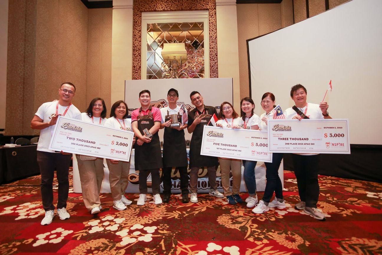Ten people hold three oversized cheques across a hotel ballroom stage
