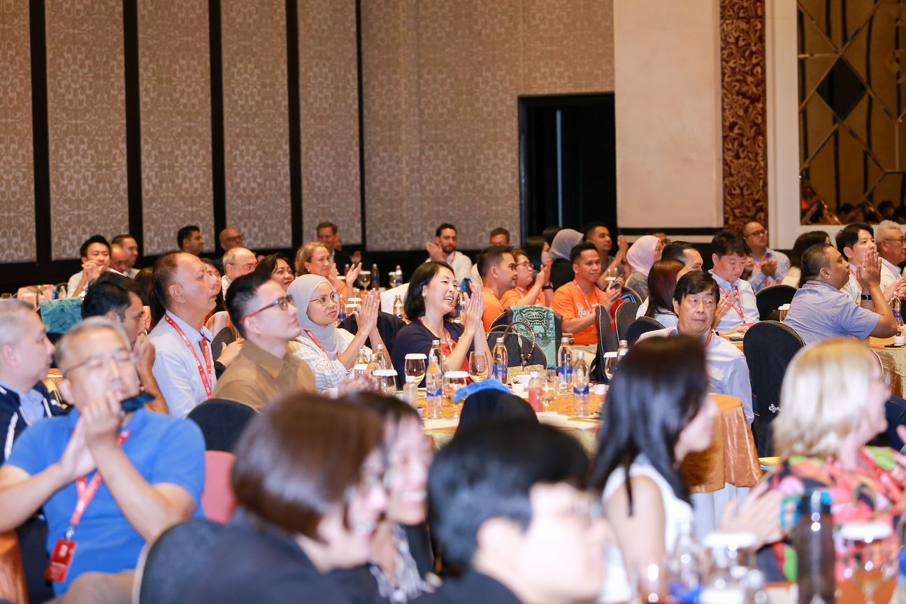 A full banquet hall applauding, one table of orange team shirts among them