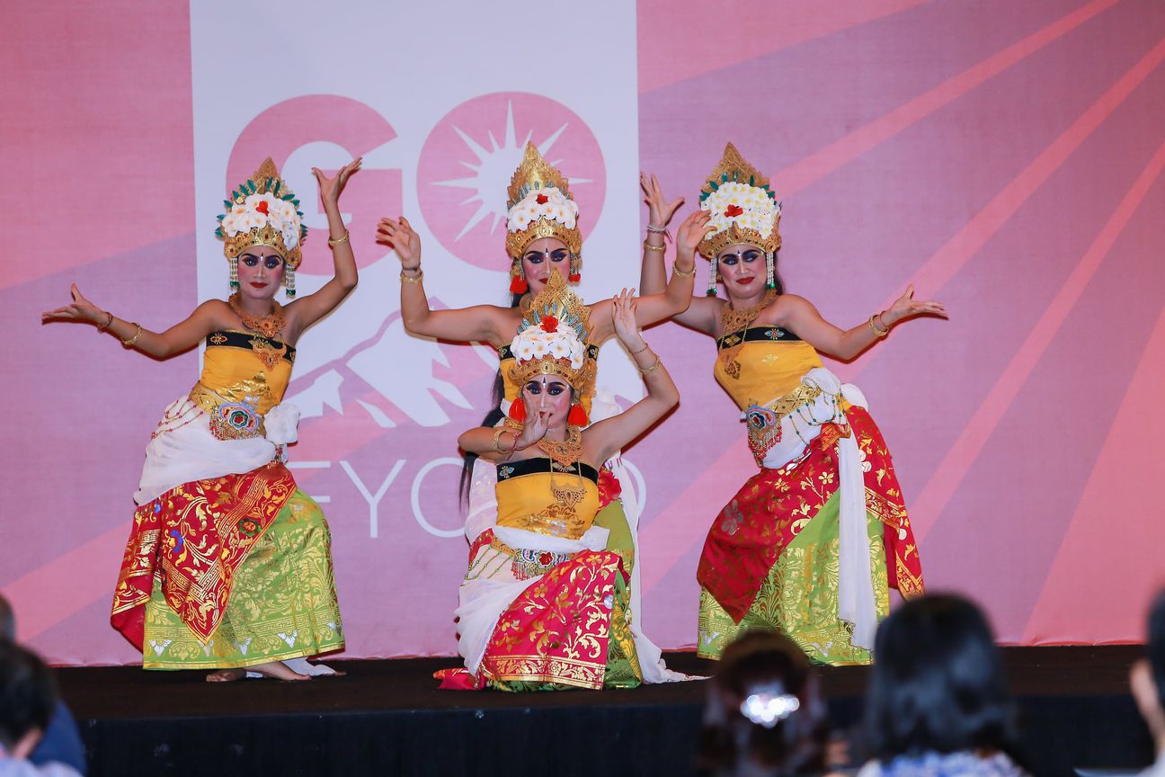 Four Balinese dancers in gold headdresses hold a pose on a lit stage