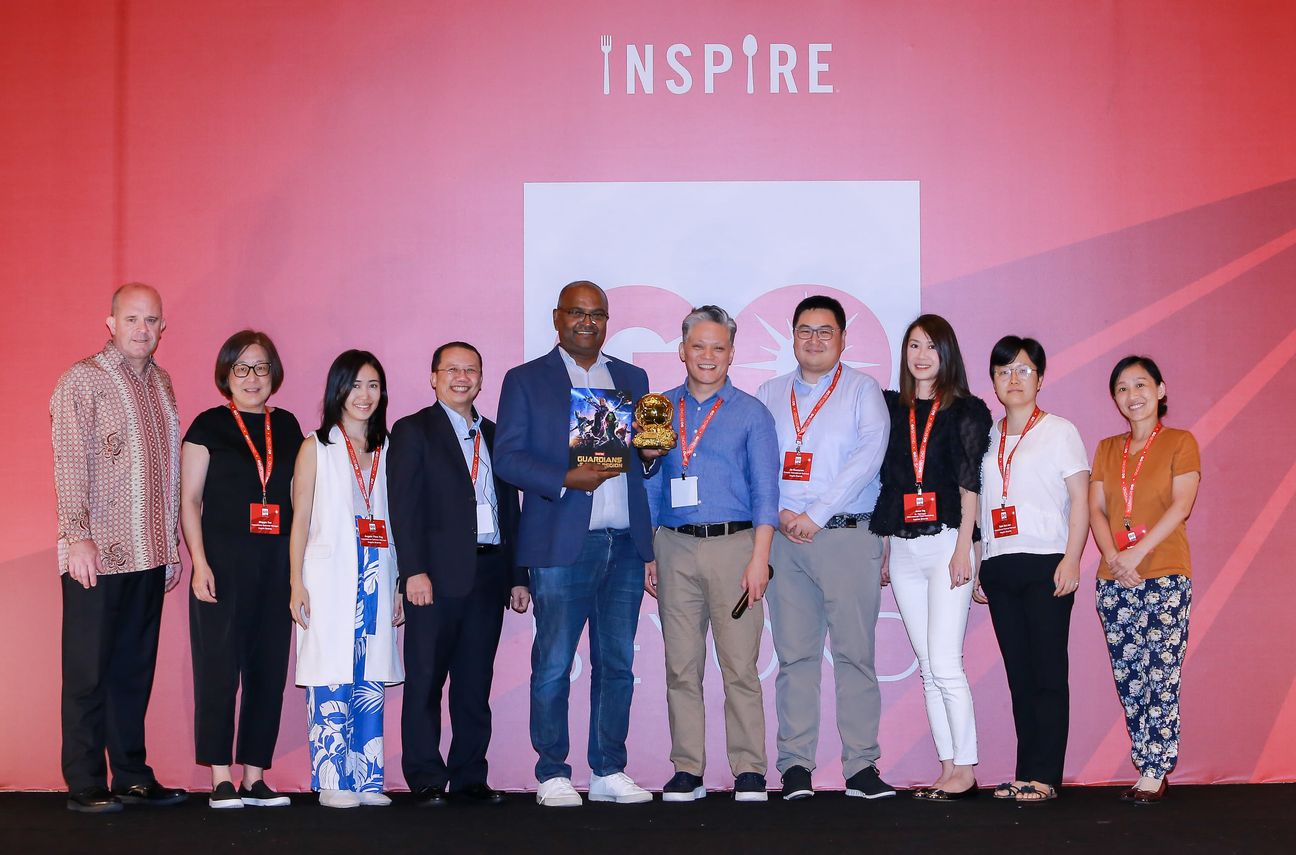 Ten colleagues stand on stage around a small gold trophy