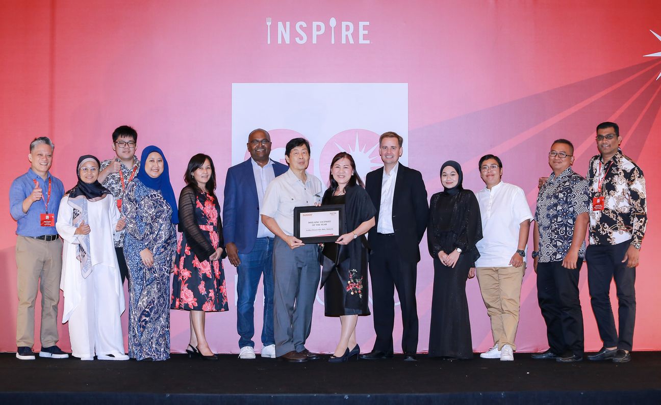 Thirteen colleagues on stage, two of them holding the framed award between them
