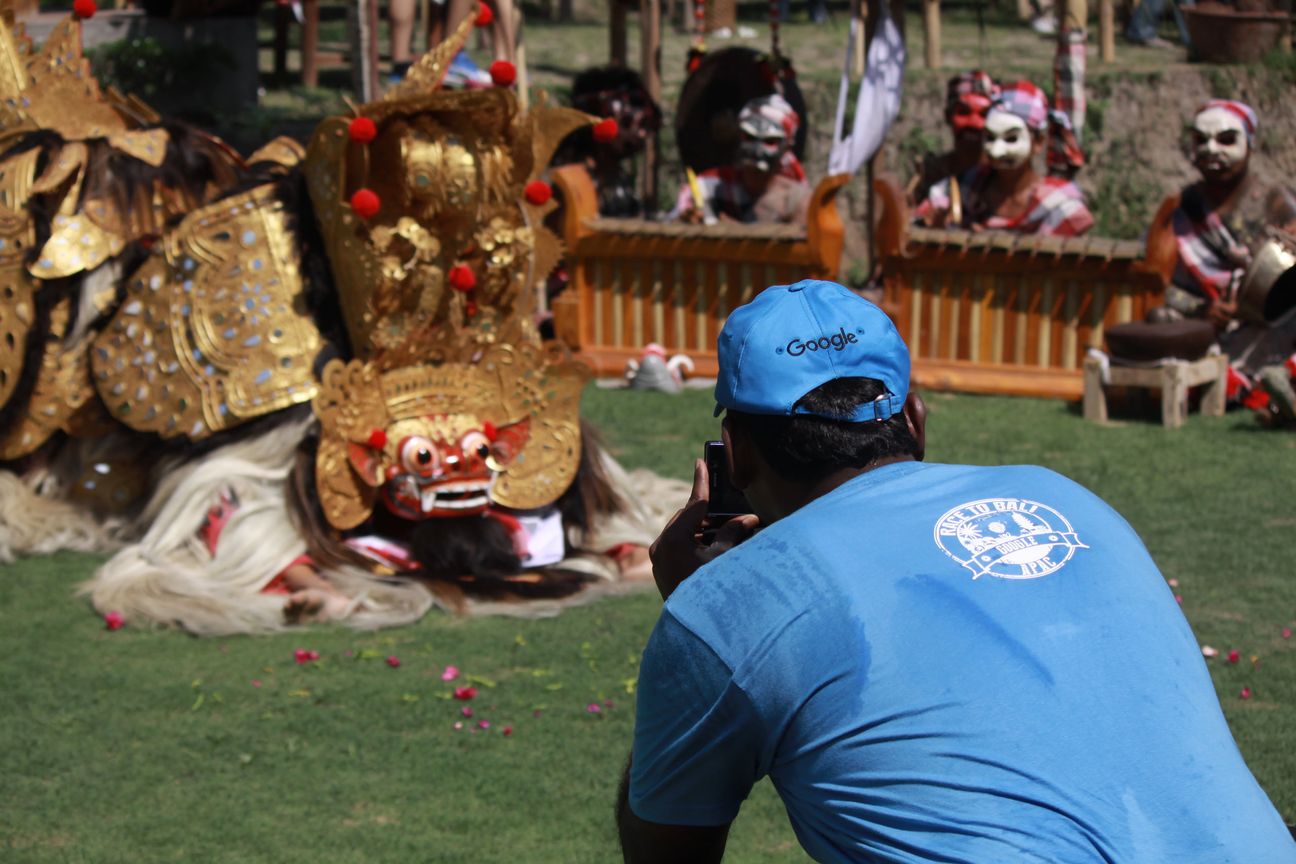 A guest crouches to photograph the Barong on the grass while the gamelan plays behind it