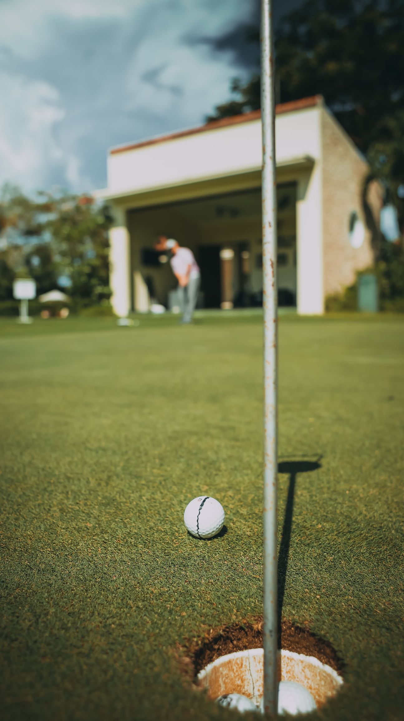 A golf ball beside the pin, the player still putting at the far end of the green