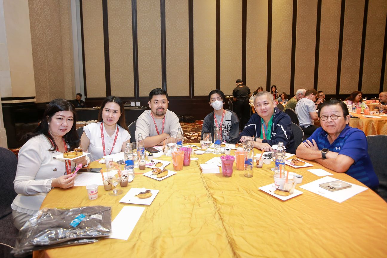Six guests turn from a table of iced coffees and doughnuts to face the camera
