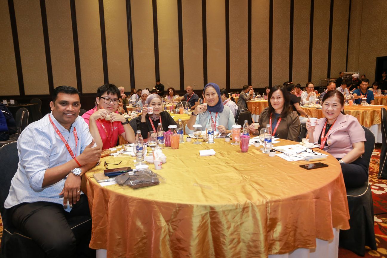 Seven guests raise iced coffees around a banquet table