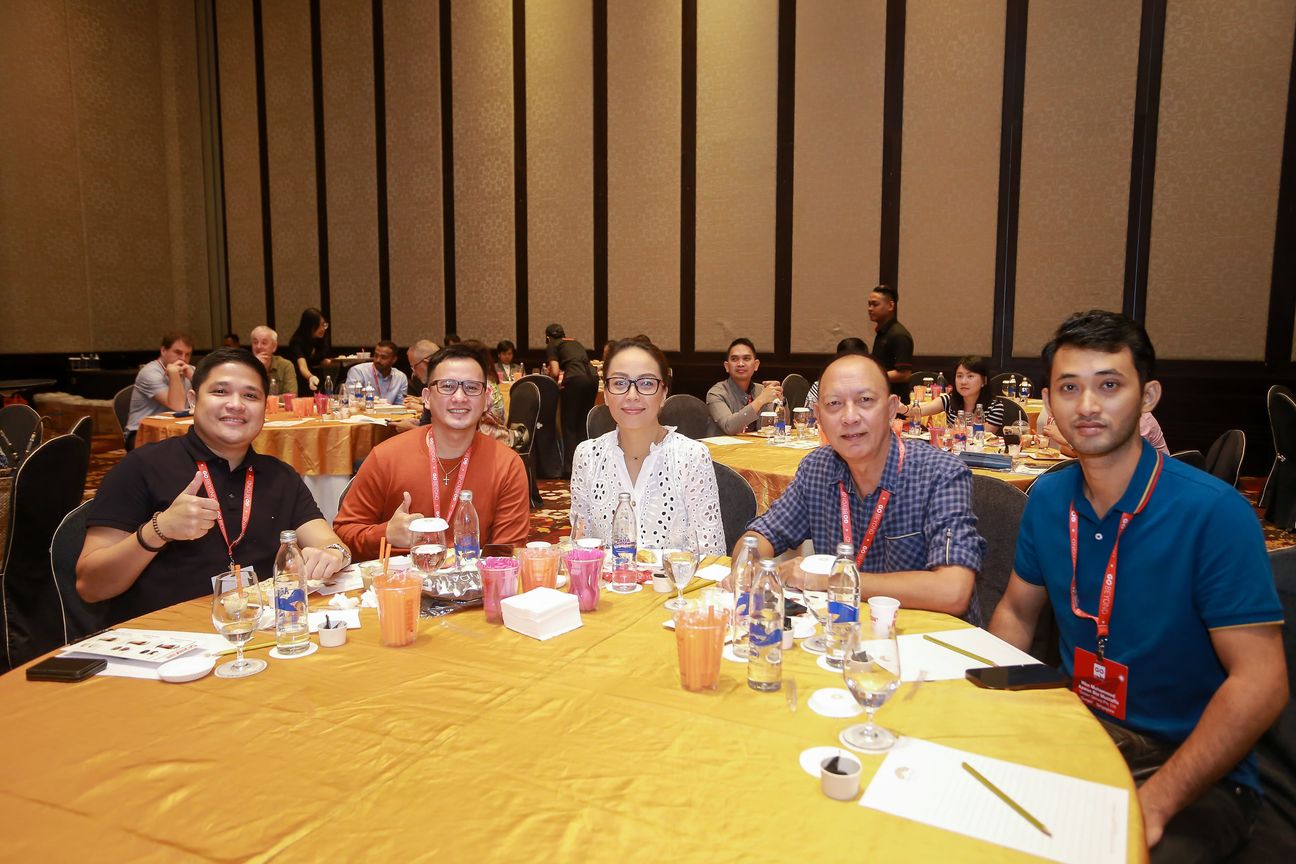 Five delegates at a banquet table, one of them giving a thumbs up