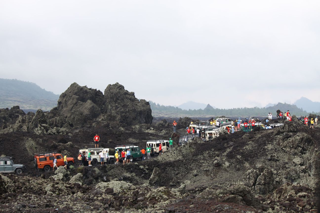 A long line of jeeps and their passengers strung out across an old lava flow