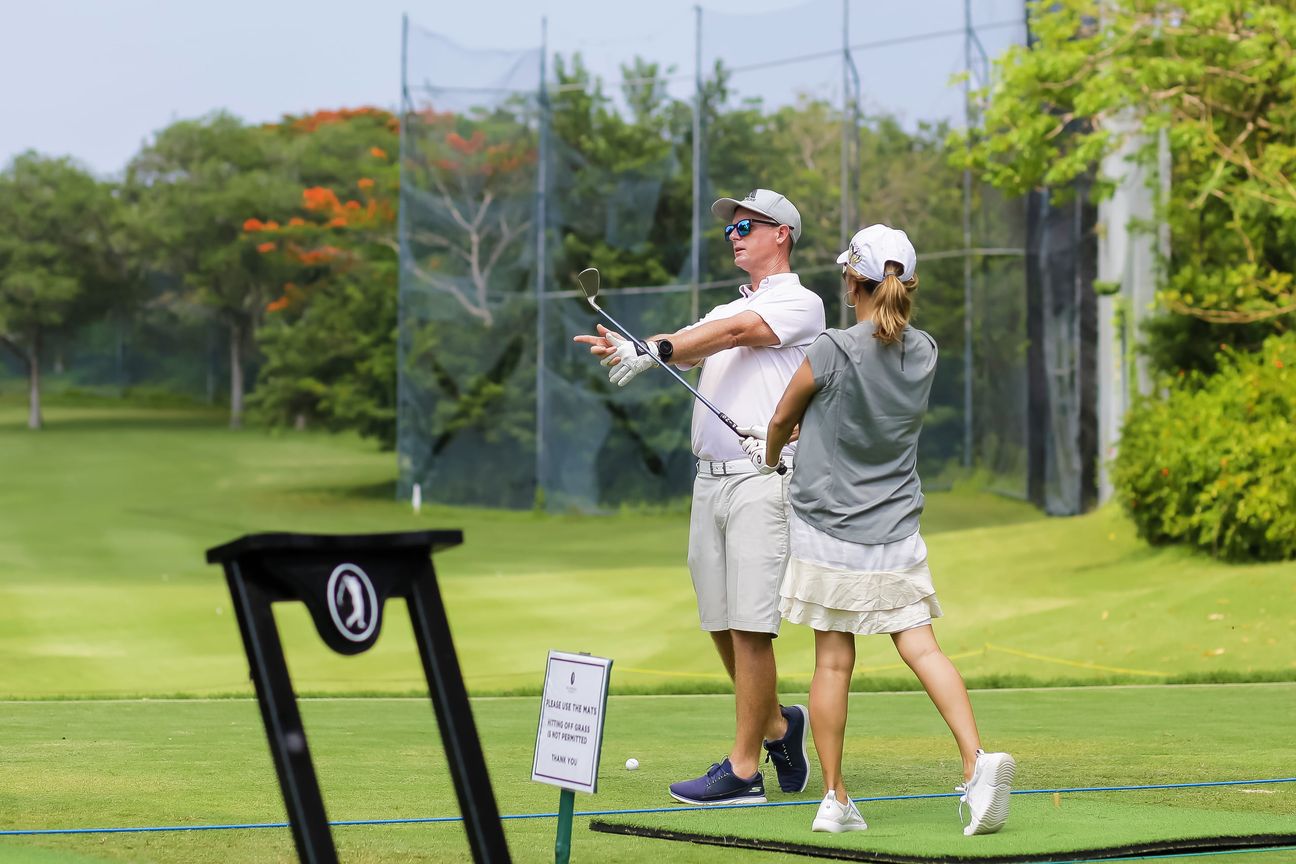 A coach gestures down the range while a golfer listens beside him