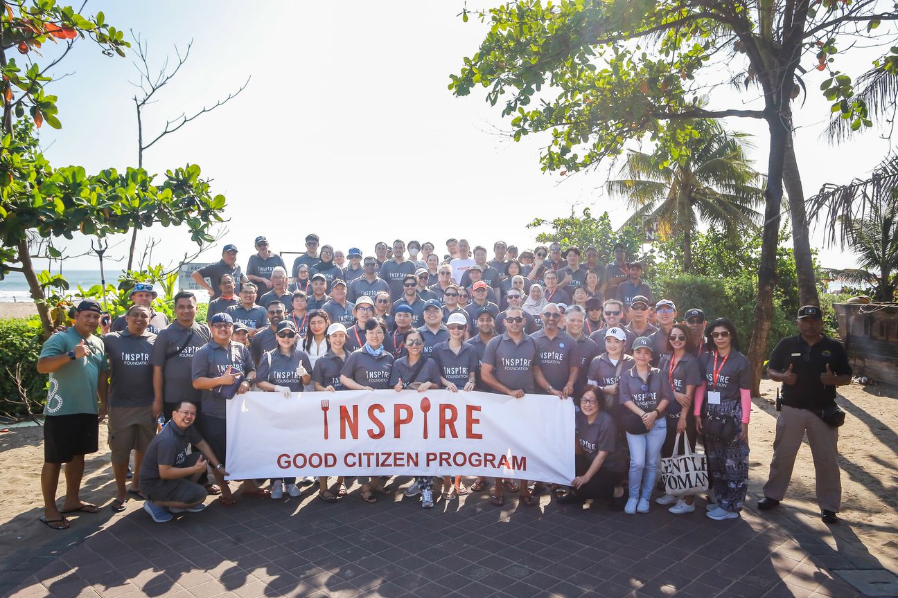 Volunteers in grey shirts fill the frame behind a banner reading Inspire Good Citizen Program